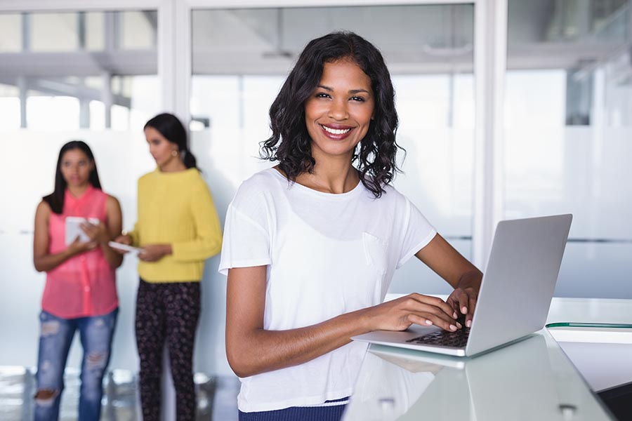 Business-Insurance-Businesswoman-Uses-Her-Laptop-at-a-High-Counter-Smiling-at-Camera-as-Employees-Work-Behind-Her